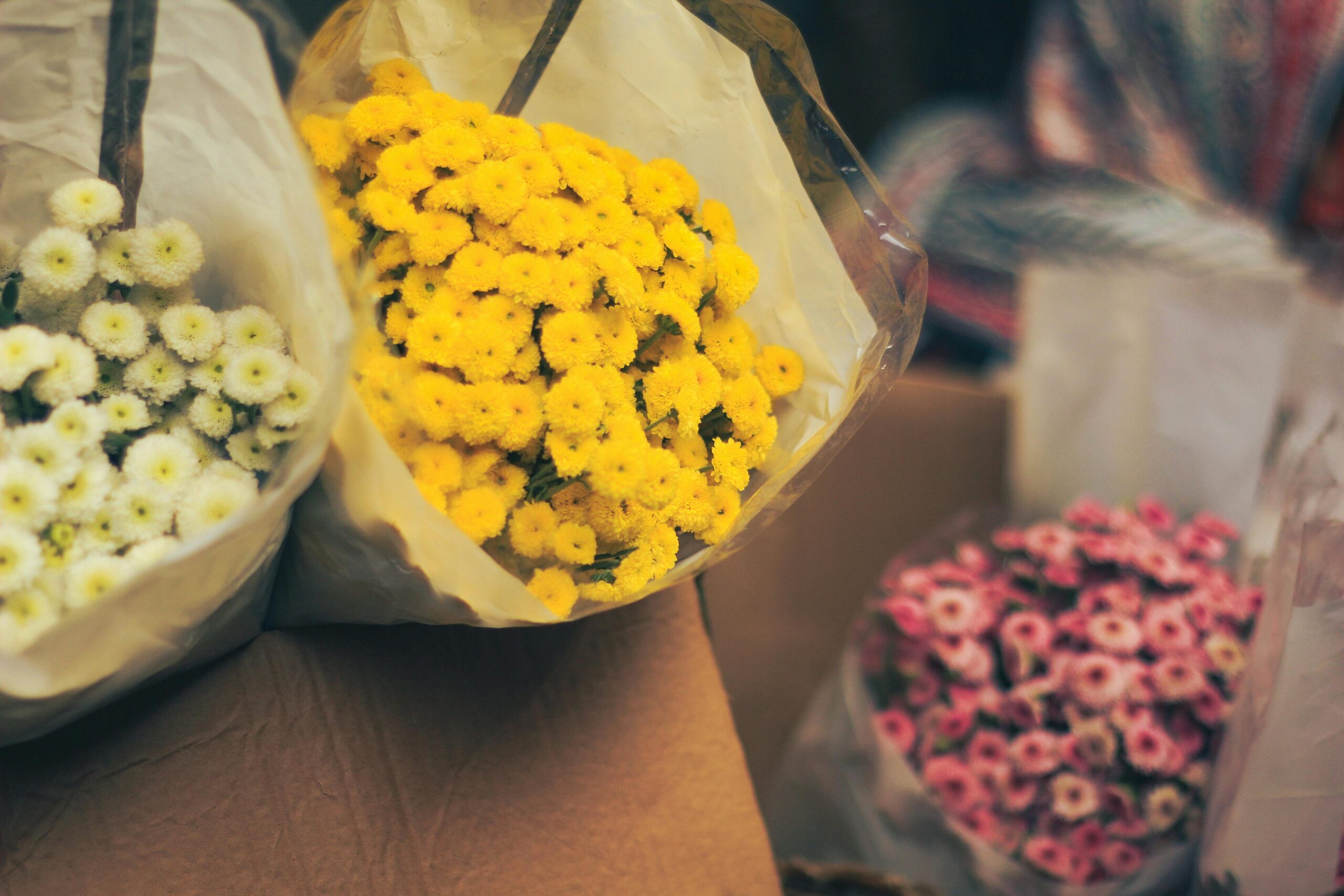 Home Colorful bouquets of pink, yellow, and white flowers wrapped in a Dhaka market setting.